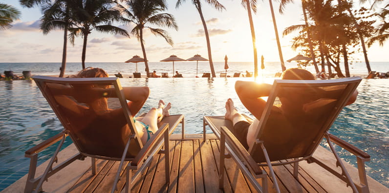 Couple Laying On Wooden Beds Next to a Pool